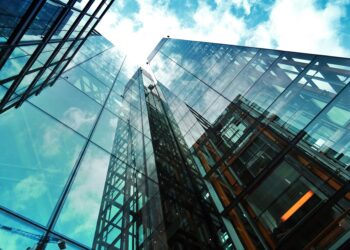 A striking view of a modern glass skyscraper reflecting the sky and clouds.